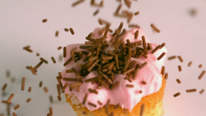 慢镜头中，巧克力屑落在了粉色的磨砂纸杯蛋糕上