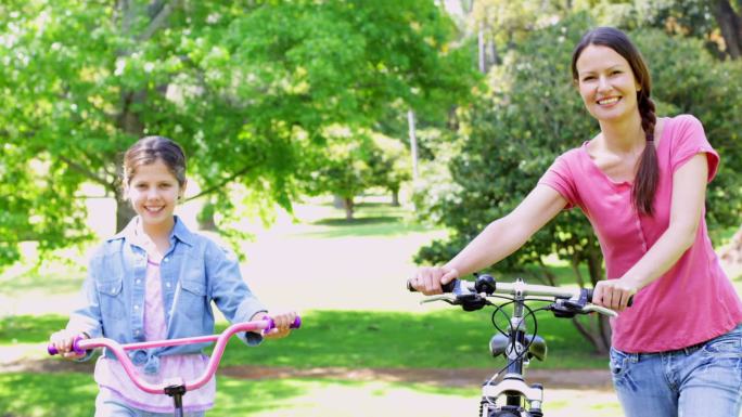 在一个阳光明媚的日子里，可爱的妈妈和女儿一起推着自行车在公园里