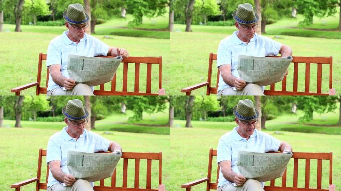 一个阳光明媚的日子，一个退休男子坐在公园的长椅上看报纸