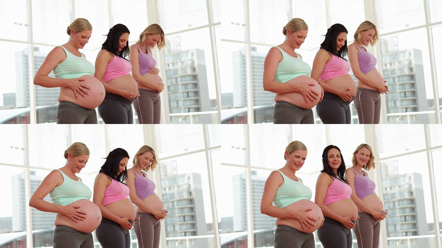 孕妇站在健身房里揉着她们的肿块