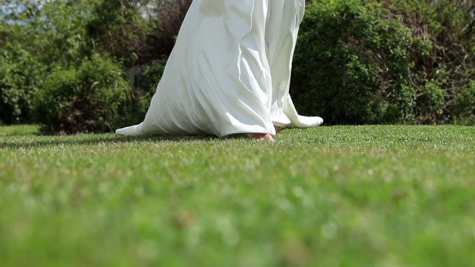 在微风中，穿着婚纱的新娘在草地上行走