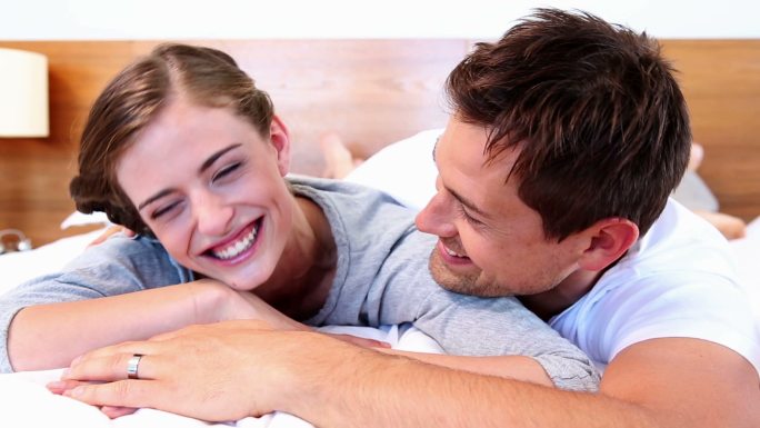 幸福的夫妻躺在床上，在家里的卧室里大笑