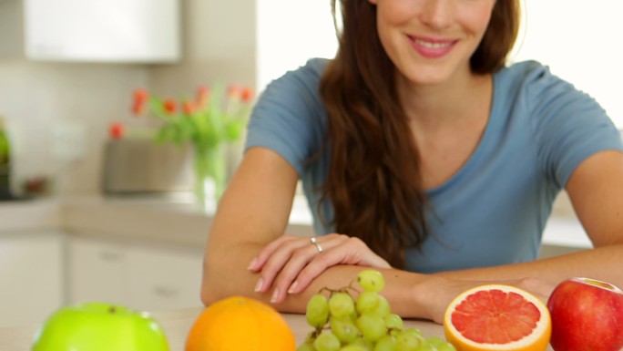 漂亮女人看着精选的水果，对着厨房里的相机竖起大拇指
