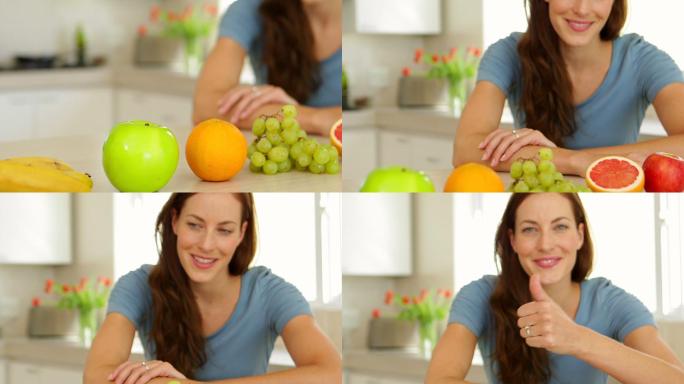 漂亮女人看着精选的水果，对着厨房里的相机竖起大拇指