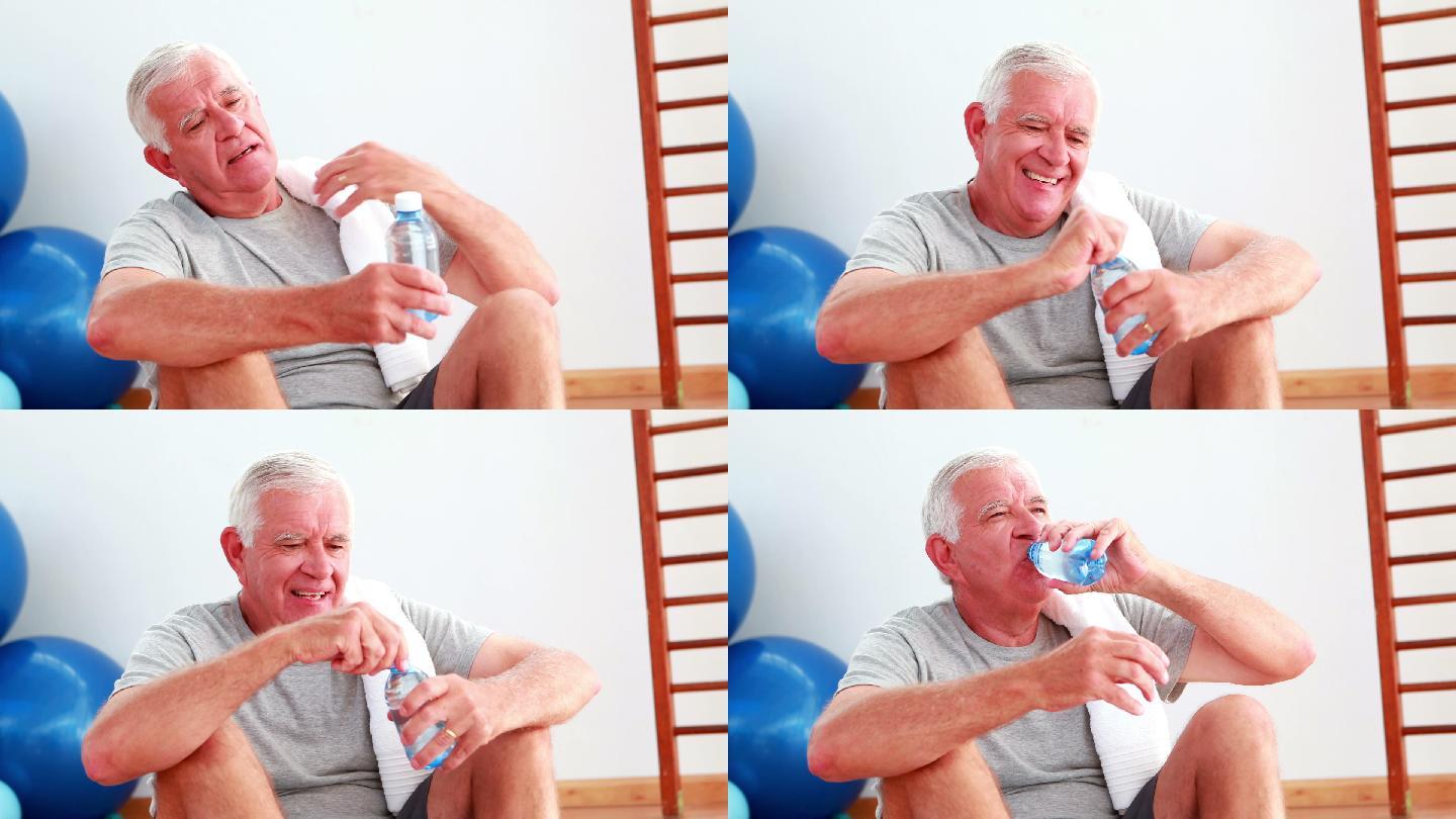 一个老人坐在健身房的地板上喝水