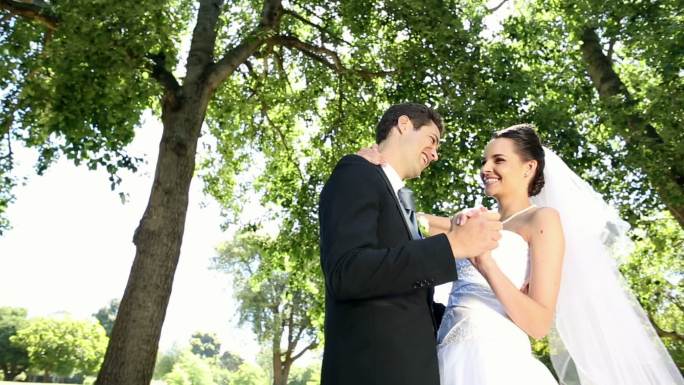 快乐的新婚夫妇在阳光明媚的日子里在公园里跳舞