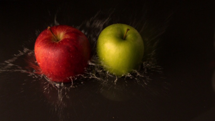 绿色和红色的苹果落在潮湿的黑色表面的慢动作