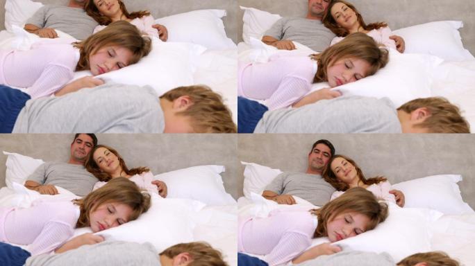 可爱的父母和孩子躺在家里的床上睡觉