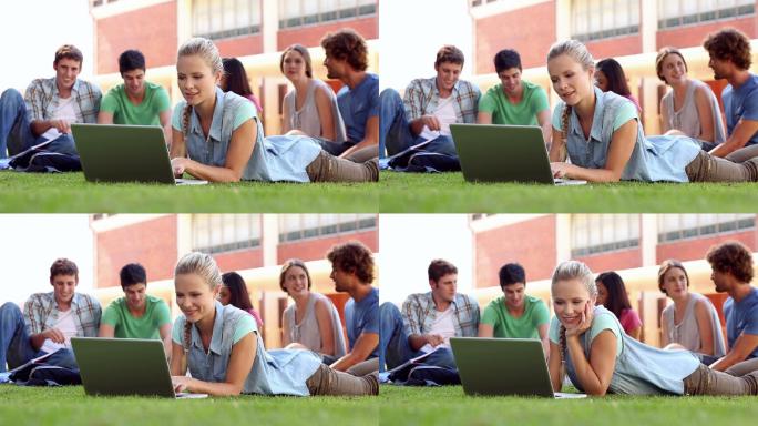 金发学生和同学坐在大学草地上使用笔记本电脑