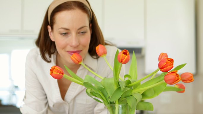 漂亮的女人闻着她的郁金香花瓶，微笑着在厨房的家里