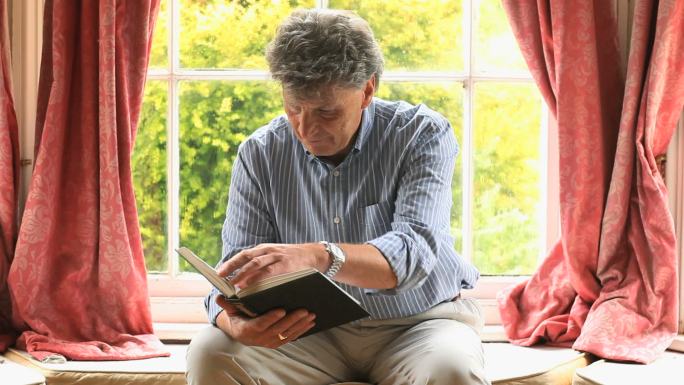 一个专注的成年人坐在客厅的窗边看书