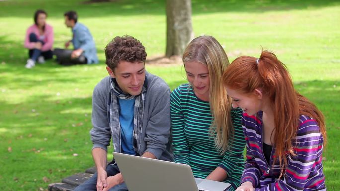 学生们在校园的草地上一起看电脑特写