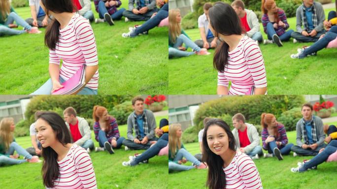 在大学的草地上，一个学生对着镜头微笑，身后是她的朋友