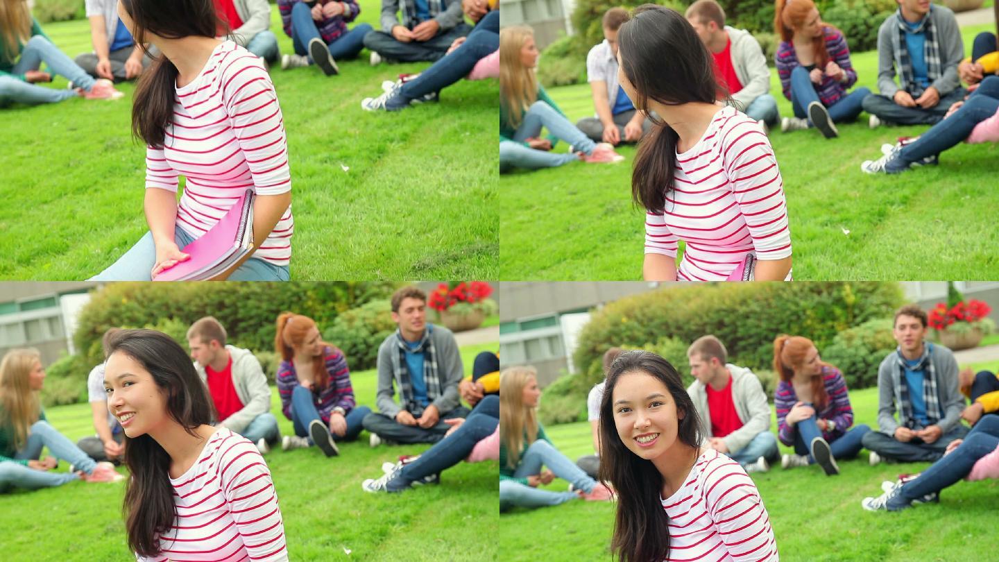 在大学的草地上，一个学生对着镜头微笑，身后是她的朋友