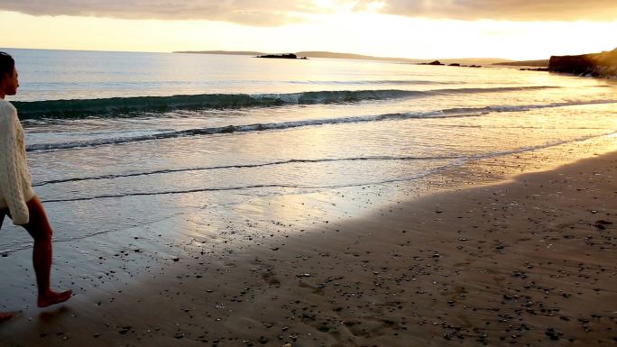 女人日落时在海滩边散步特写