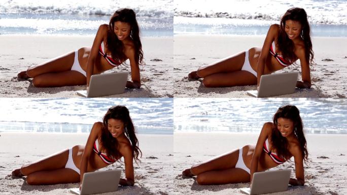 迷人的女人在比基尼放松与她的笔记本电脑在海滩上