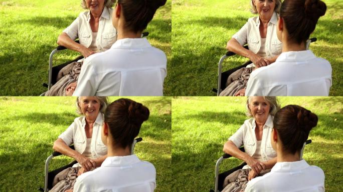 一个阳光明媚的日子，护士在外面和一个坐轮椅的女人说话