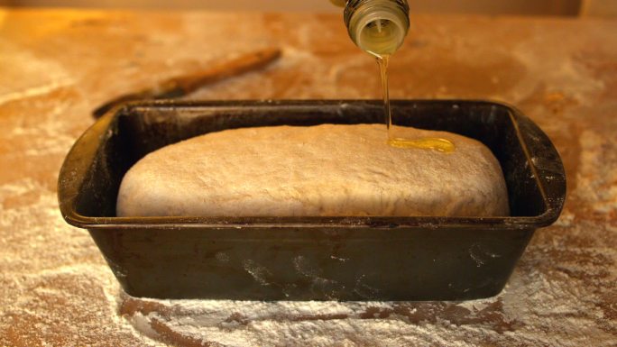 用慢镜头将橄榄油倒在面粉桌上的面包盒中的生面团上