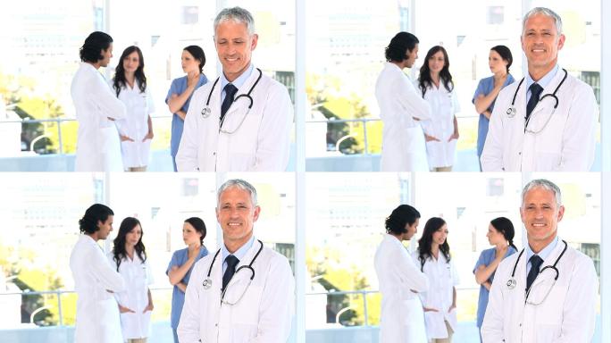 微笑着成熟的医生站在他的团队前面，在一个明亮的房间里