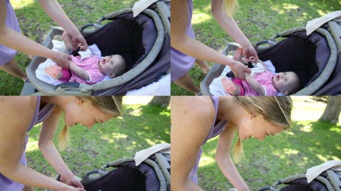 在一个阳光明媚的日子里，母亲在公园里推着婴儿车照顾她的小女儿