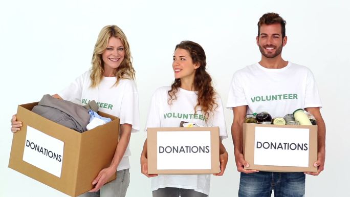 一群志愿者拿着捐款箱在白色背景下对着镜头微笑