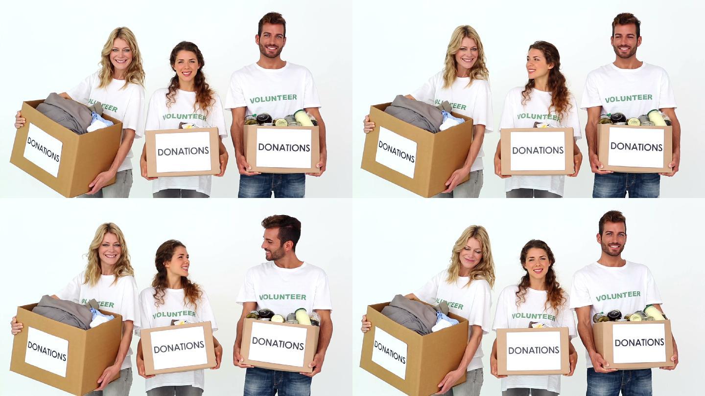 一群志愿者拿着捐款箱在白色背景下对着镜头微笑