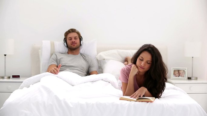 女人在床上看书，而伴侣在听音乐