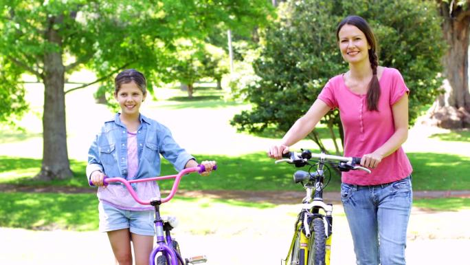 可爱的妈妈和女儿在一个阳光明媚的日子里一起在公园里骑自行车