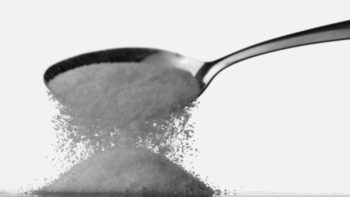 用勺子将糖粉倒在白色背景上的一堆糖上