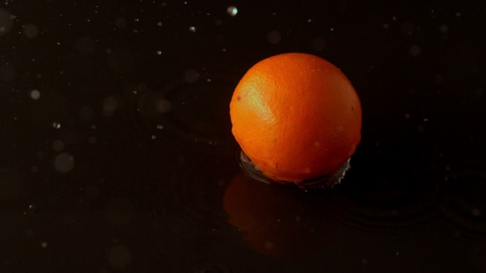 在慢镜头中，橙色滴在潮湿的黑色表面上
