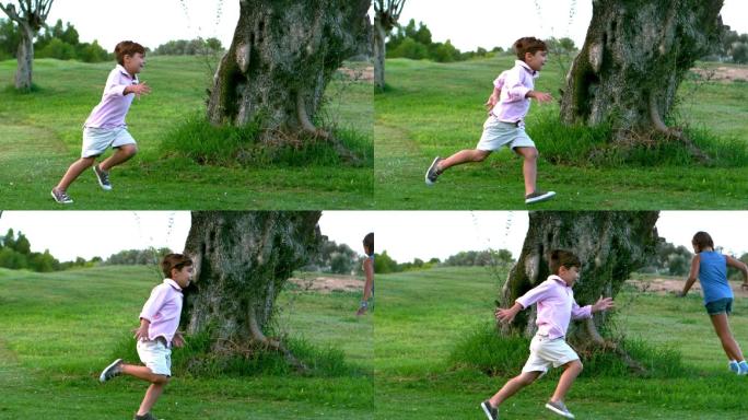 一个小男孩和妹妹绕着一棵大树跑的慢镜头