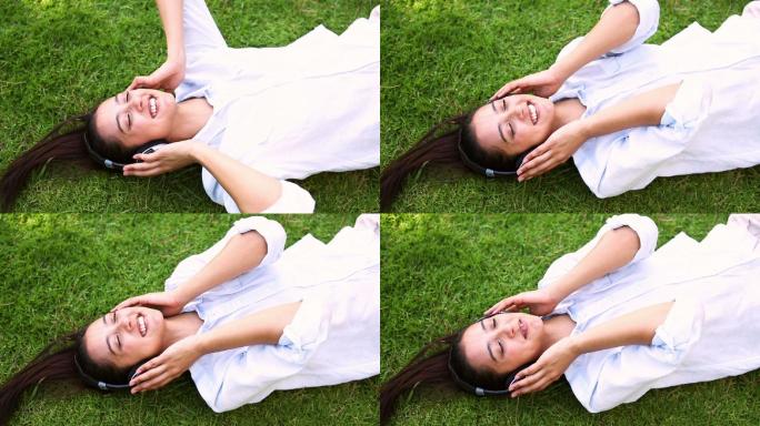 在一个阳光明媚的日子里，一个漂亮的女孩躺在草地上听音乐