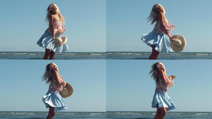 迷人的金发女郎拿着草帽在沙滩上慢镜头旋转