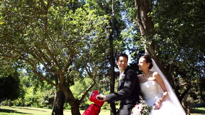快乐的新婚夫妇在一个阳光明媚的日子里在公园里骑着一辆红色的摩托车