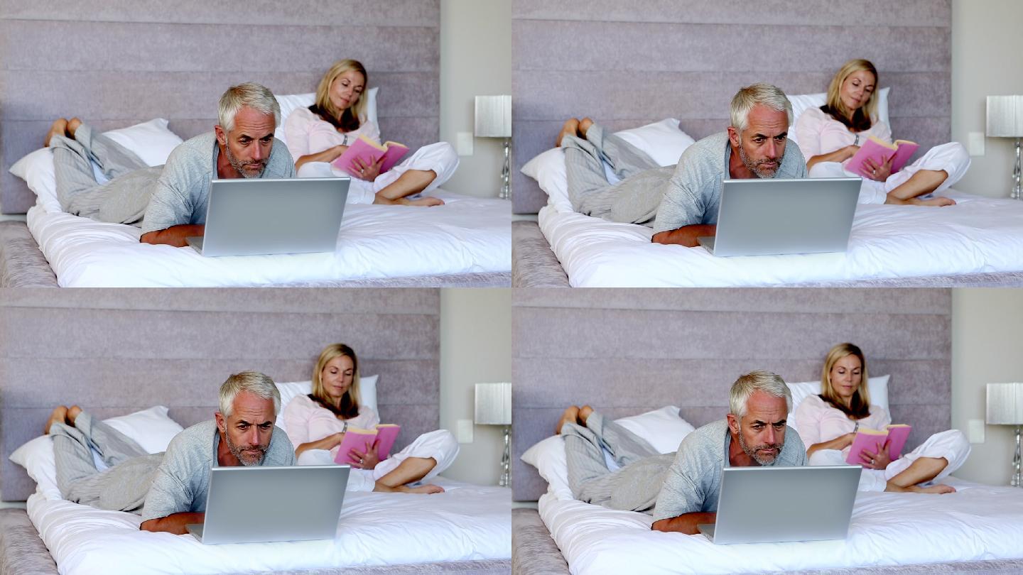 一个男人躺在床上，旁边放着一台笔记本电脑，他的妻子正在看书