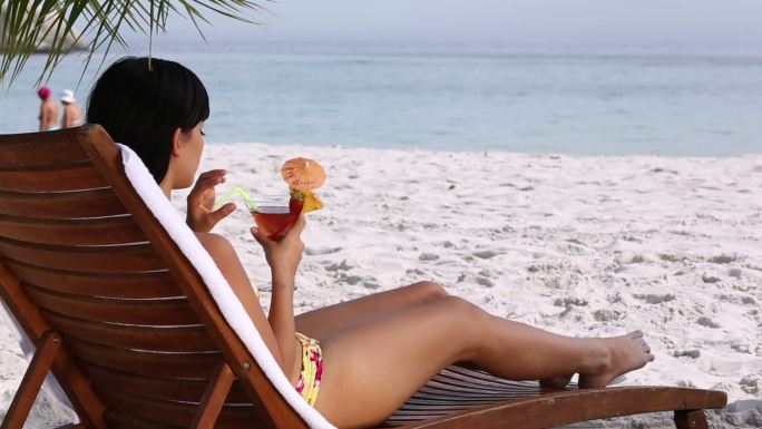 女人在沙滩上的椅子上喝鸡尾酒特写