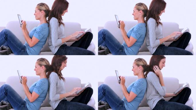 两个朋友坐在沙发上，一边看书一边用平板电脑
