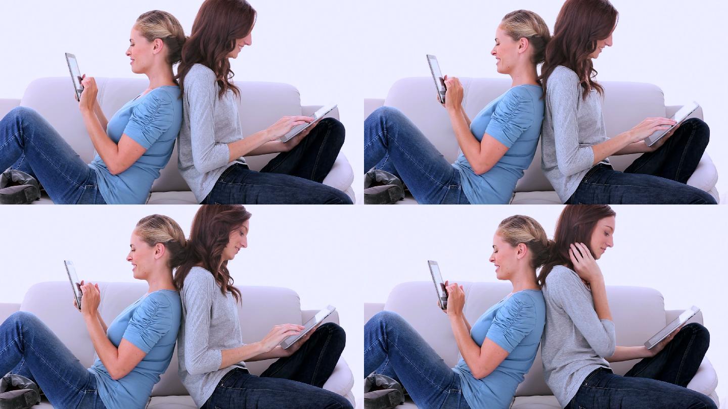 两个朋友坐在沙发上，一边看书一边用平板电脑