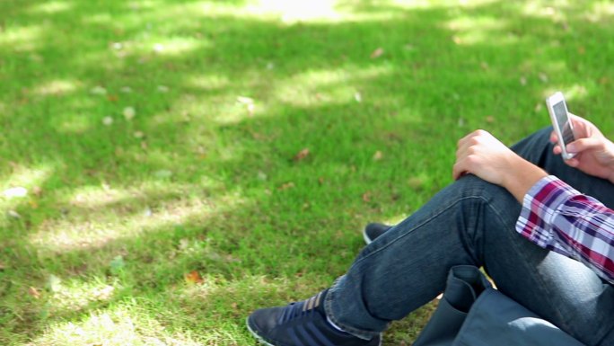 一个男生坐在草地上看手机特写