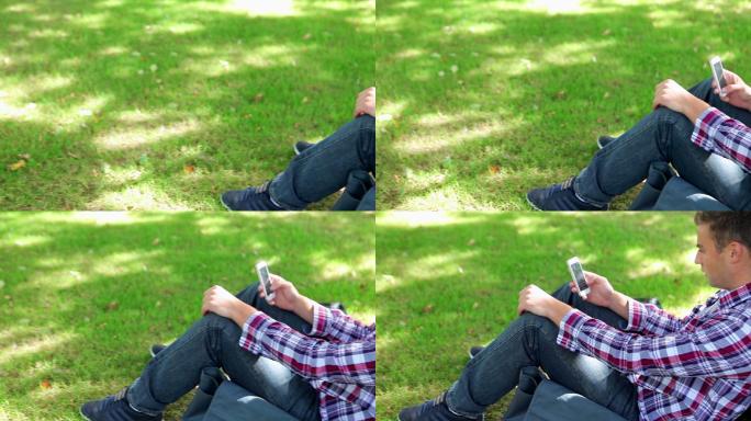 一个男生坐在草地上看手机特写
