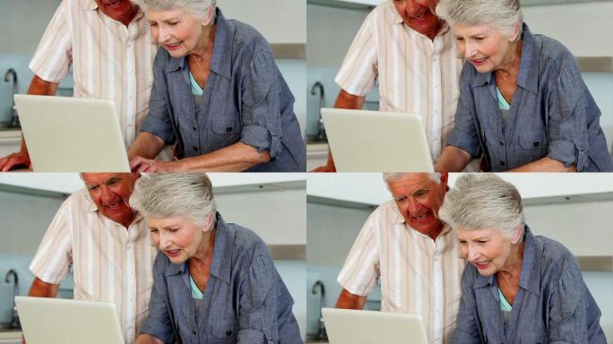 一对老年夫妇在厨房的柜台上使用笔记本电脑