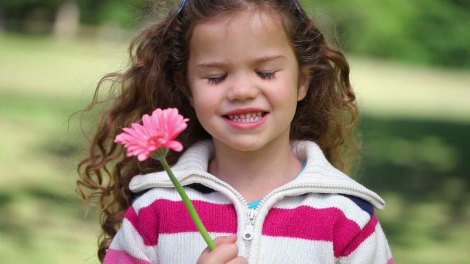 小女孩站在公园里展示一朵粉红色的花