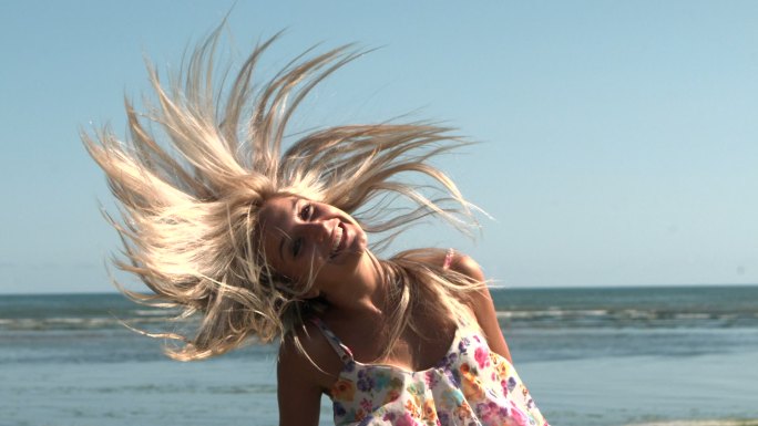 慢镜头里，快乐的金发女郎在沙滩上摇晃头发