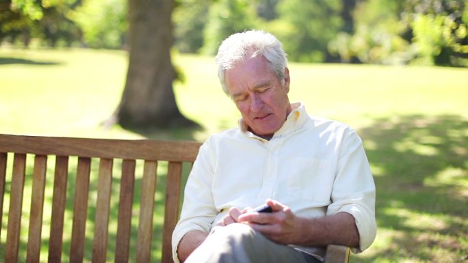 一个退休男子坐在公园的长椅上用手机特写