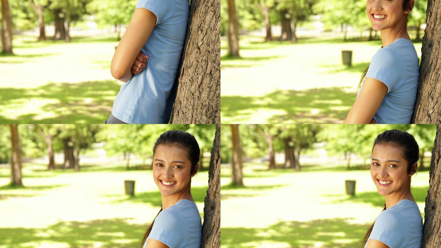 在一个阳光明媚的日子里，一个健康的女孩倚在公园的树上