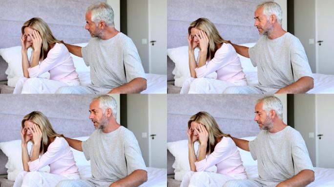 丈夫在床上安慰他的妻子，而她的头夹在她的双手之间
