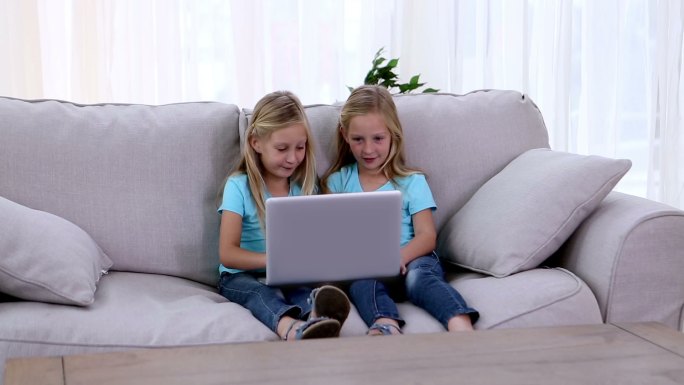 两姐妹在沙发上玩笔记本电脑