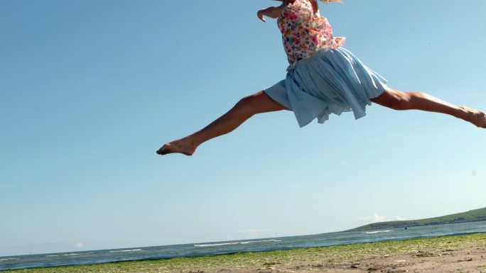 美丽的金发女郎在沙滩上做芭蕾跳慢动作