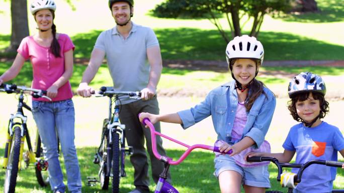 在一个阳光明媚的日子里，一家人微笑着在公园里骑自行车
