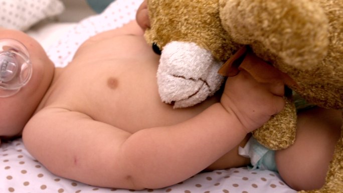 婴儿躺在婴儿床上吮吸奶嘴，抱着泰迪熊的慢镜头
